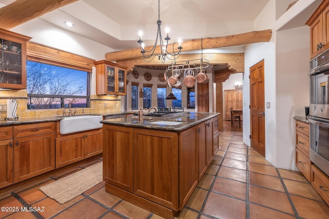 kitchen with pendant lighting, sink, decorative backsplash, a kitchen island with sink, and stainless steel double oven