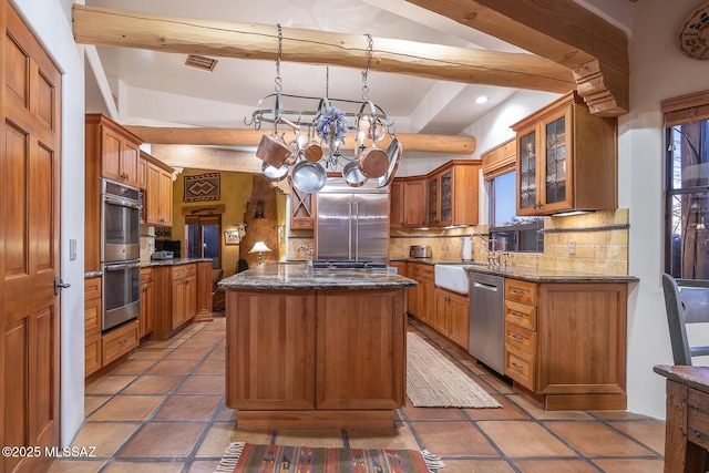 kitchen featuring appliances with stainless steel finishes, decorative light fixtures, a kitchen island, and dark stone countertops