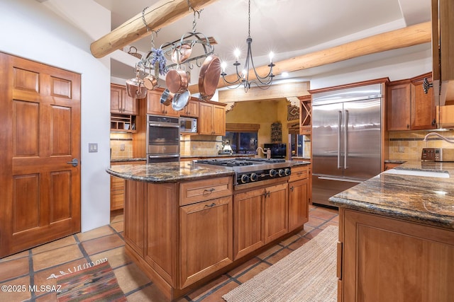 kitchen featuring tasteful backsplash, built in appliances, decorative light fixtures, a kitchen island, and dark stone counters