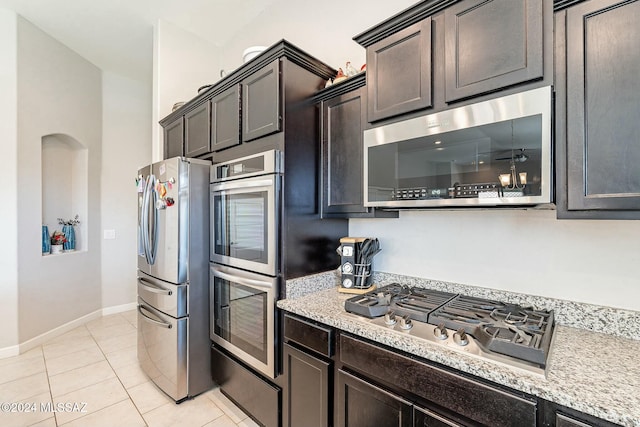 kitchen with light stone countertops, appliances with stainless steel finishes, dark brown cabinets, and light tile patterned flooring