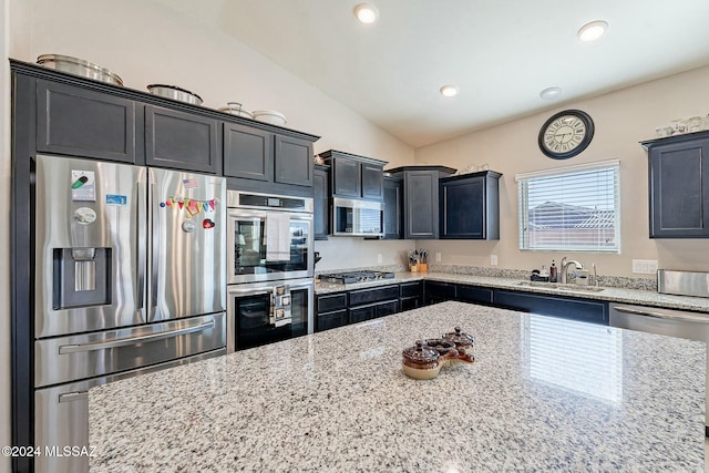 kitchen with light stone countertops, stainless steel appliances, vaulted ceiling, and sink