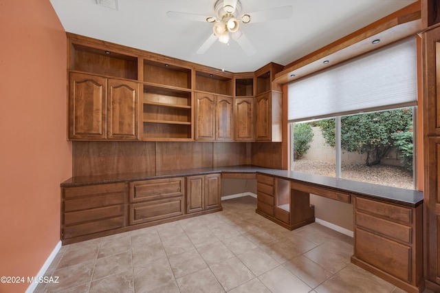 unfurnished office with ceiling fan, light tile patterned flooring, and built in desk