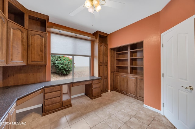 unfurnished office featuring ceiling fan, built in desk, and light tile patterned floors