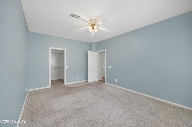 unfurnished bedroom featuring a walk in closet, ceiling fan, a closet, and light carpet