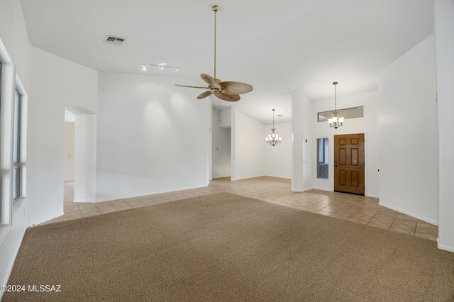 unfurnished living room with a towering ceiling, ceiling fan with notable chandelier, and light colored carpet