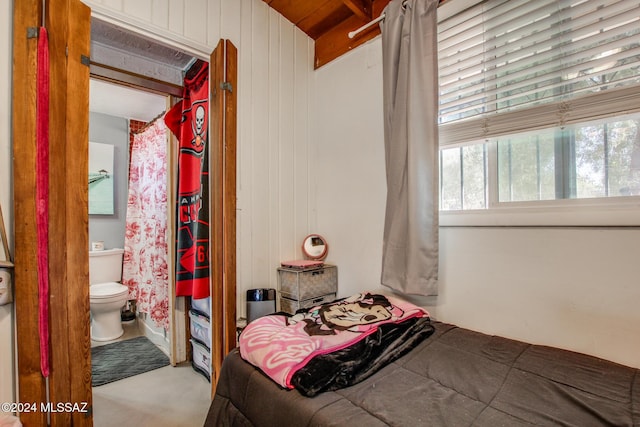 carpeted bedroom featuring beamed ceiling, ensuite bathroom, and wooden walls