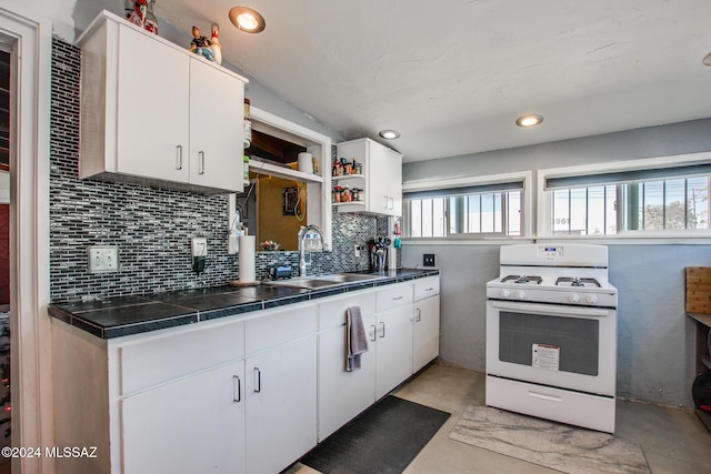 kitchen featuring white cabinets, decorative backsplash, white range with gas cooktop, and sink