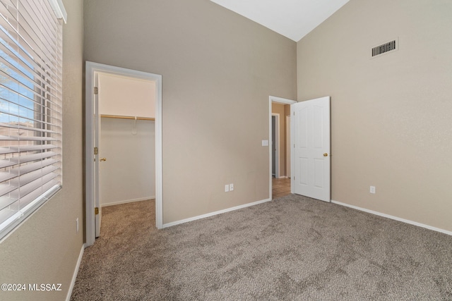 unfurnished bedroom featuring a walk in closet, a closet, carpet, and high vaulted ceiling