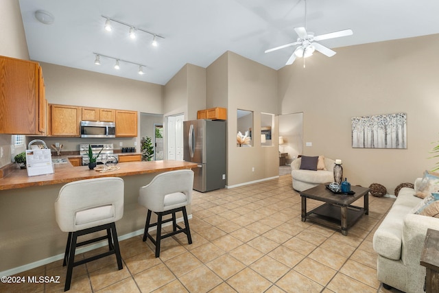 kitchen featuring kitchen peninsula, appliances with stainless steel finishes, ceiling fan, a high ceiling, and a breakfast bar area