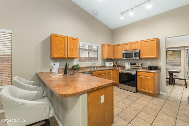 kitchen with high vaulted ceiling, sink, light tile patterned floors, appliances with stainless steel finishes, and kitchen peninsula