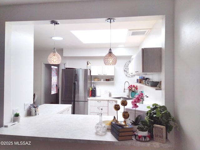 kitchen with white cabinetry, stainless steel fridge, sink, and hanging light fixtures