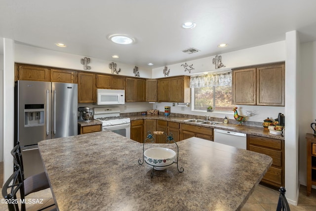 kitchen featuring sink, white appliances, light tile patterned floors, a kitchen breakfast bar, and a center island