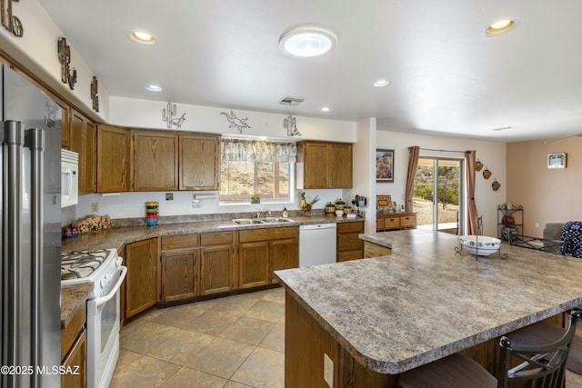 kitchen with sink, white appliances, a breakfast bar area, light tile patterned floors, and a center island