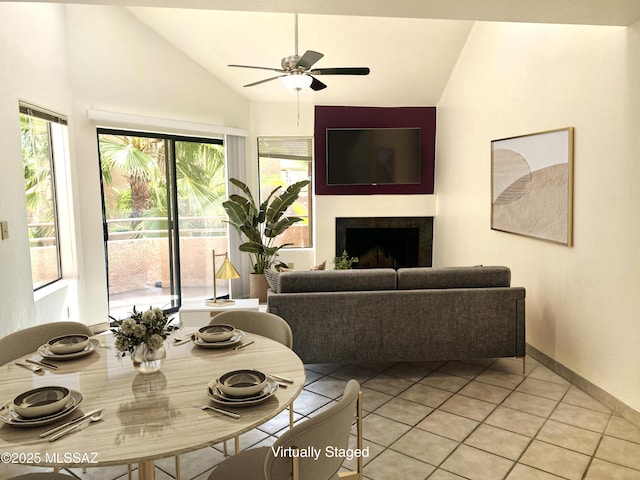 living area with a fireplace, a ceiling fan, light tile patterned flooring, vaulted ceiling, and baseboards