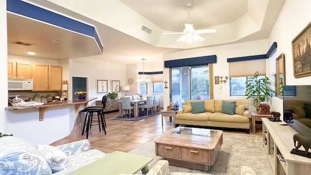 living room with ceiling fan with notable chandelier, light tile patterned floors, and a tray ceiling