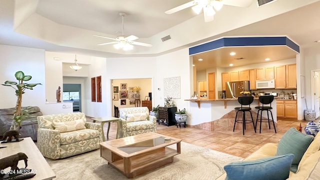 tiled living room with ceiling fan, a raised ceiling, and a high ceiling