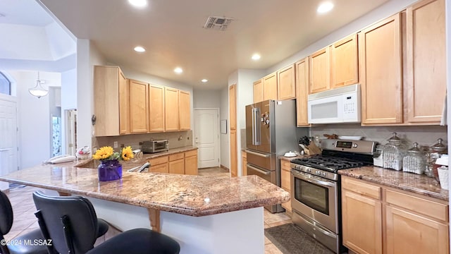 kitchen with light stone countertops, stainless steel range with gas cooktop, light brown cabinetry, decorative backsplash, and a breakfast bar