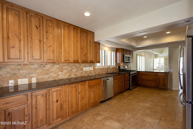 kitchen with brown cabinets, a sink, appliances with stainless steel finishes, dark countertops, and tasteful backsplash