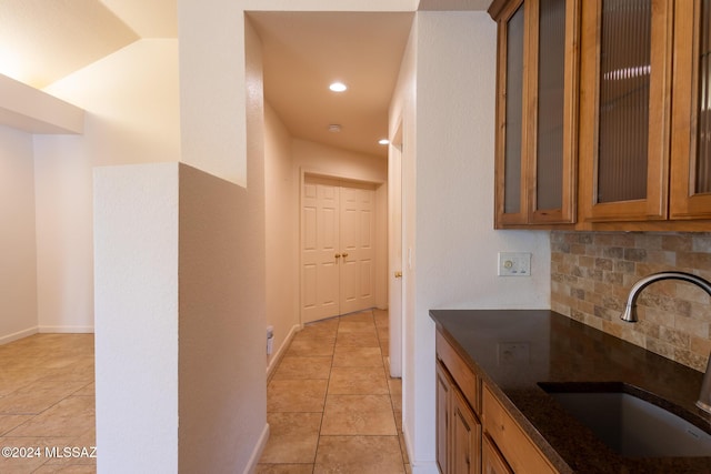 kitchen featuring decorative backsplash, light tile patterned flooring, sink, and dark stone counters