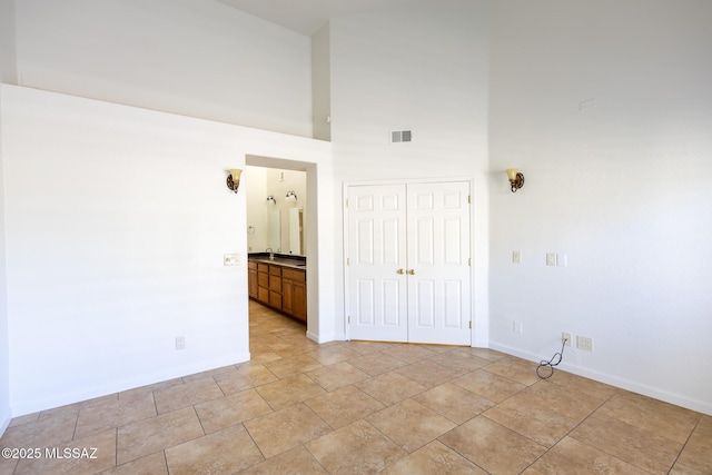 unfurnished room with light tile patterned floors, baseboards, visible vents, and a towering ceiling