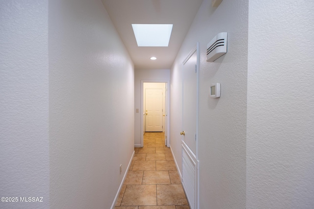 hall with baseboards, a skylight, and light tile patterned flooring