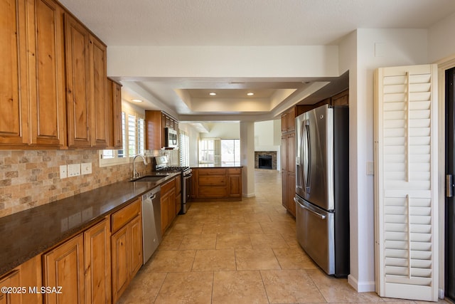 kitchen with a tray ceiling, a fireplace, stainless steel appliances, decorative backsplash, and brown cabinets