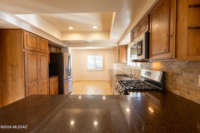 kitchen with sink, tasteful backsplash, dark stone countertops, a tray ceiling, and appliances with stainless steel finishes