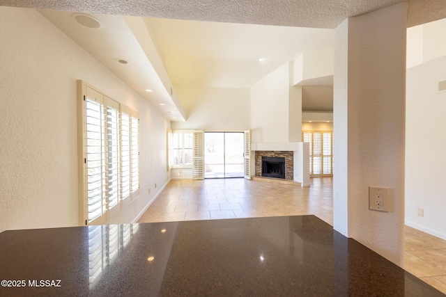 unfurnished living room with a textured ceiling, a fireplace, light tile patterned floors, baseboards, and a textured wall