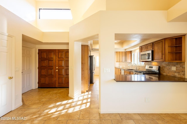 kitchen featuring sink, tasteful backsplash, kitchen peninsula, light tile patterned floors, and appliances with stainless steel finishes