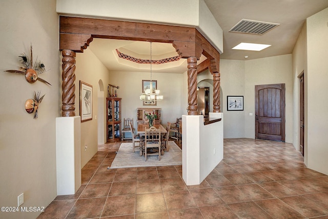 hallway with tile patterned floors, decorative columns, an inviting chandelier, and a tray ceiling