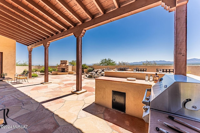 view of patio with a mountain view, area for grilling, and an outdoor fireplace