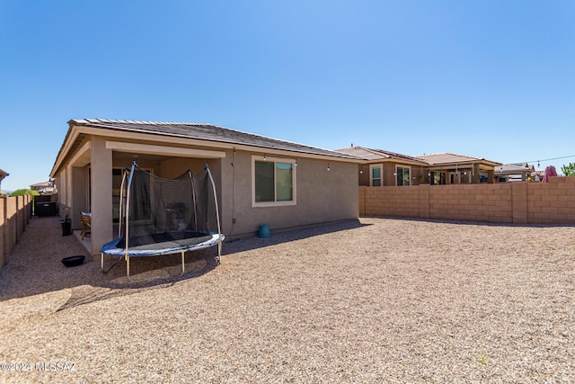 back of property with a trampoline, a fenced backyard, and stucco siding