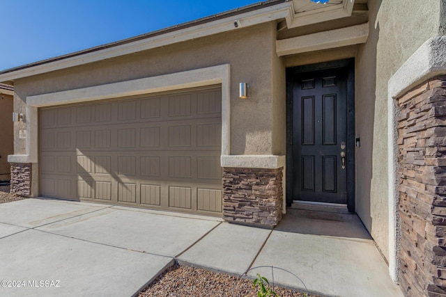 property entrance with a garage, stone siding, concrete driveway, and stucco siding