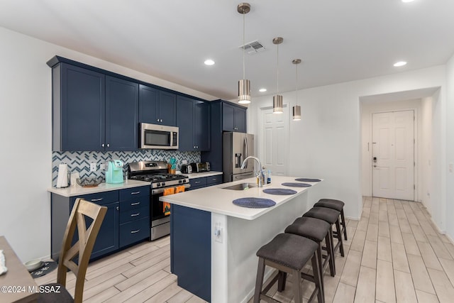 kitchen with appliances with stainless steel finishes, blue cabinets, a kitchen island with sink, decorative light fixtures, and a breakfast bar area