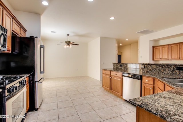 kitchen featuring ceiling fan, light tile patterned floors, appliances with stainless steel finishes, and dark stone counters