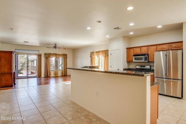 kitchen with ceiling fan, stainless steel appliances, dark stone countertops, a kitchen island with sink, and light tile patterned flooring