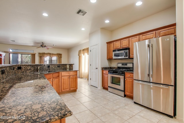 kitchen featuring dark stone counters, sink, ceiling fan, light tile patterned floors, and stainless steel appliances