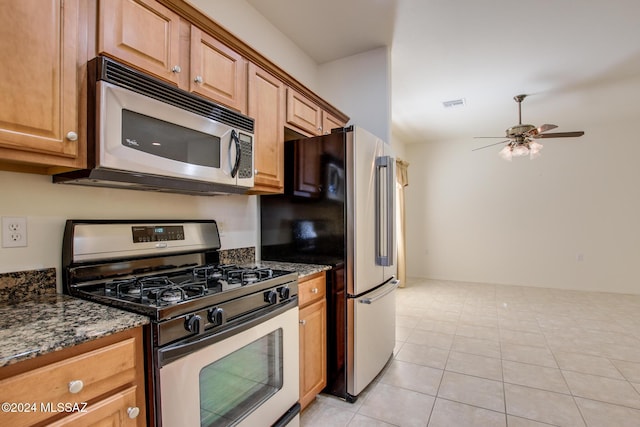 kitchen with ceiling fan, light tile patterned floors, stainless steel appliances, and dark stone counters