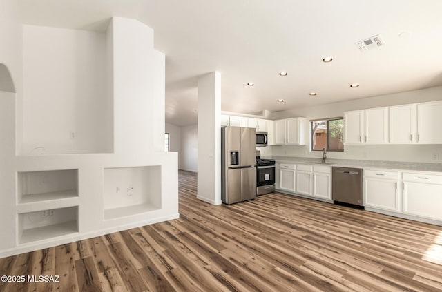 kitchen featuring visible vents, light wood-type flooring, white cabinets, stainless steel appliances, and a sink