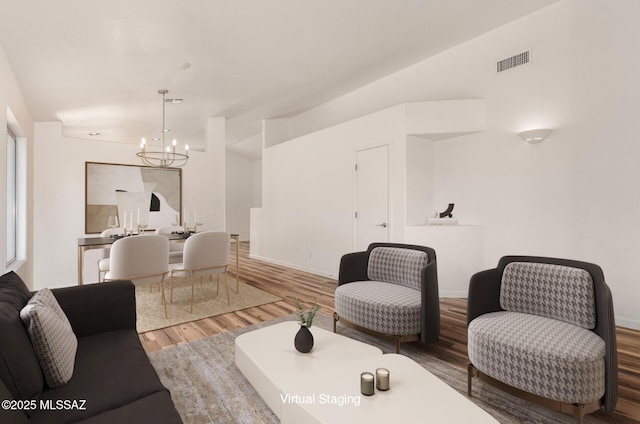 living area featuring visible vents, lofted ceiling, an inviting chandelier, and wood finished floors