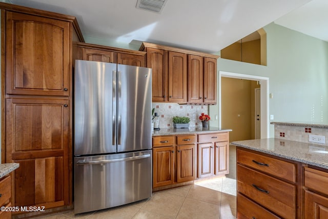 kitchen featuring backsplash, stainless steel refrigerator, light stone counters, and light tile patterned floors