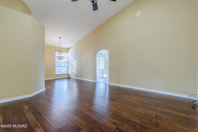 empty room featuring ceiling fan with notable chandelier, high vaulted ceiling, and dark hardwood / wood-style floors