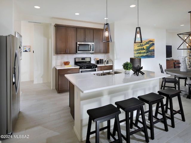 kitchen with appliances with stainless steel finishes, sink, decorative light fixtures, light hardwood / wood-style floors, and a breakfast bar area