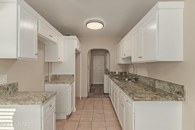 kitchen featuring light tile patterned floors, light stone counters, white cabinetry, and sink