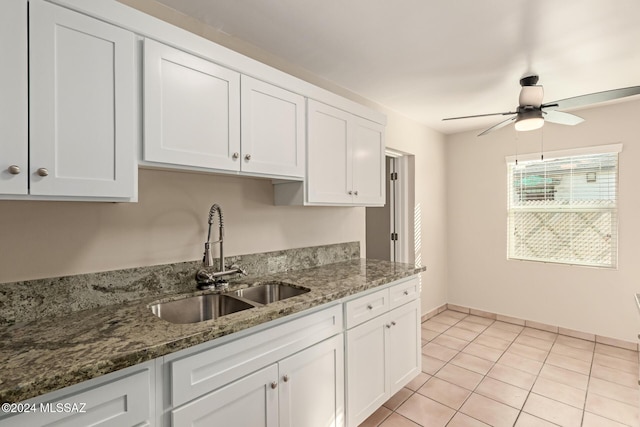 kitchen with white cabinets, light tile patterned flooring, dark stone counters, and sink