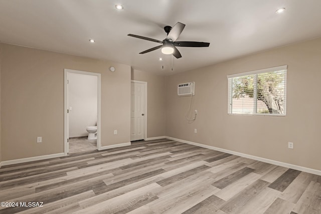 unfurnished bedroom featuring light wood-type flooring, ensuite bathroom, a wall mounted AC, ceiling fan, and a closet