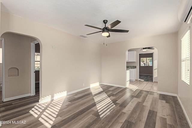 unfurnished living room featuring dark hardwood / wood-style floors, an AC wall unit, and ceiling fan