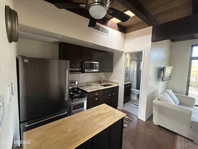 kitchen featuring appliances with stainless steel finishes, dark brown cabinets, ceiling fan, sink, and beamed ceiling