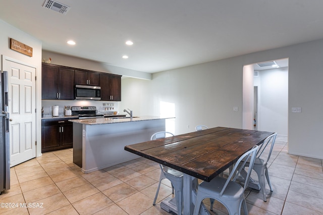 kitchen with an island with sink, light tile patterned floors, and appliances with stainless steel finishes