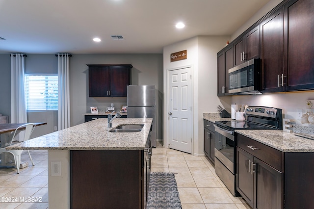 kitchen featuring sink, light tile patterned floors, an island with sink, light stone counters, and stainless steel appliances